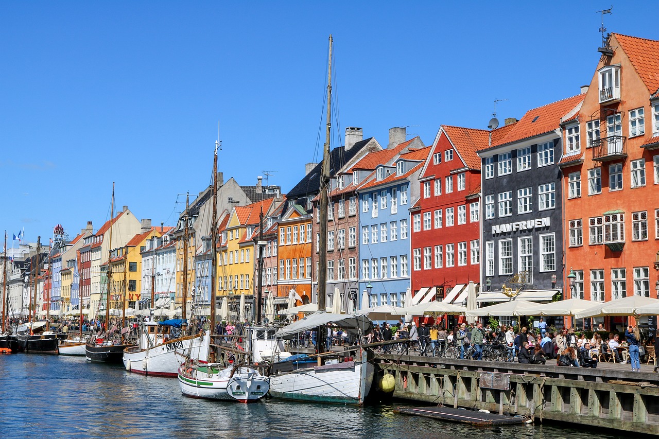 Colorful buildings along the iconic Nyhavn canal in Copenhagen, Denmark, reflecting in the calm waters under a clear blue sky.