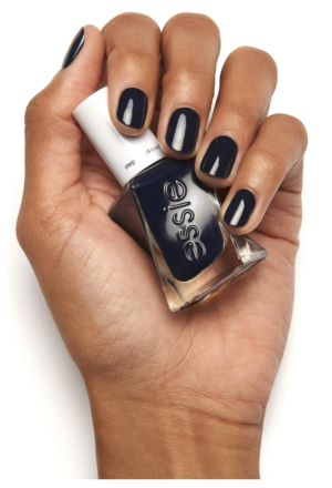 woman's hand holding an Essie nail polish bottle with finger nails painted with navy blue nail polish against a white background.