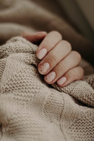 white woman's hand under a beige blanket with finger nails painted nude color with gold polka dot design.