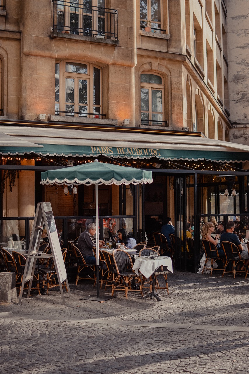 Paris cafe with green awning and umbrella and beige Parisian building with people sitting outside on the terrace at tables with white table cloths
