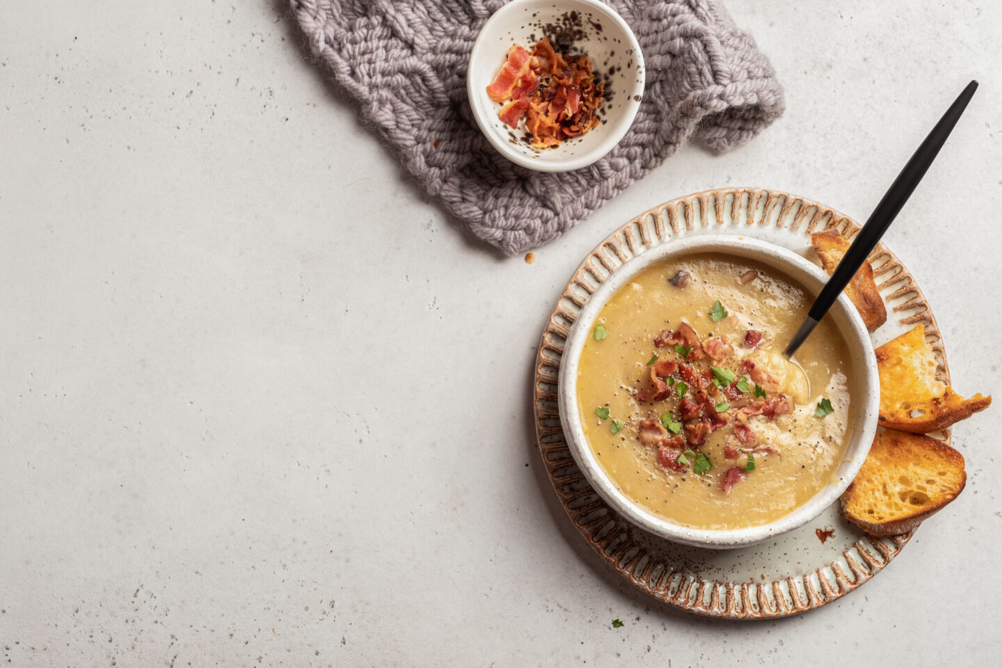 bowl of soup topped with bacon, side of crust bread, bowl of extra bacon bits on top of a napkin