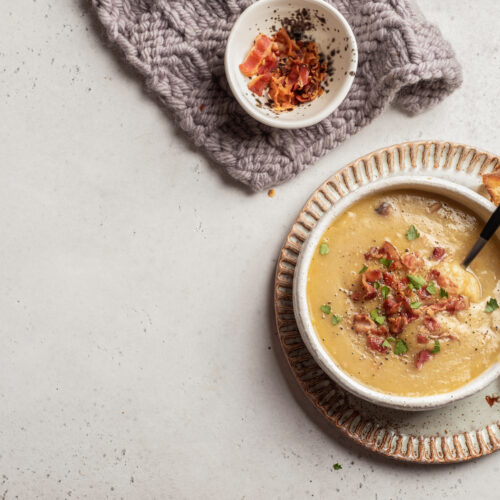 bowl of soup topped with bacon, side of crust bread, bowl of extra bacon bits on top of a napkin