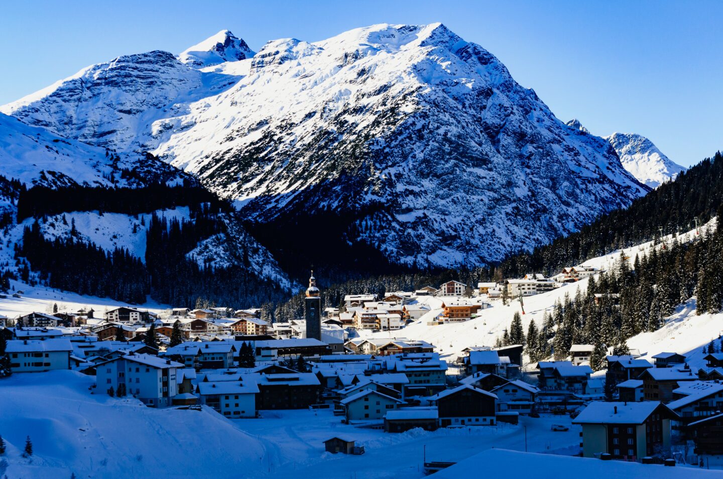 snow covered ski village in valley between snow covered mountains with blue sky in background