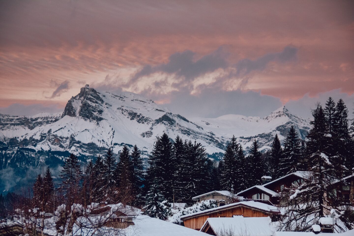 ski tow in europe pink sky sunset over mountain town covered in snow with mountains and trees in Megève france