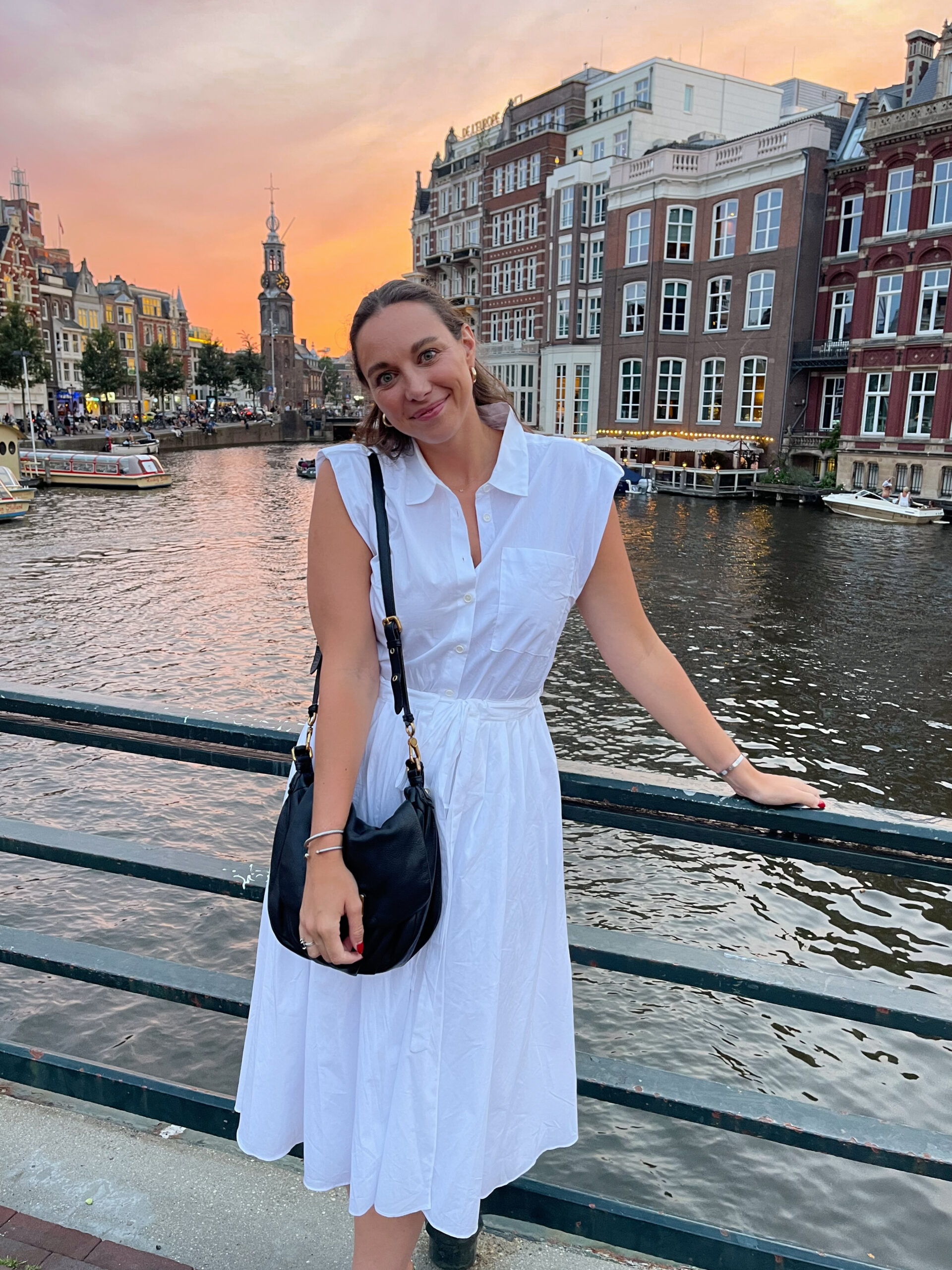 woman in white dress standing on bridge over canal in amsterdam at sunset