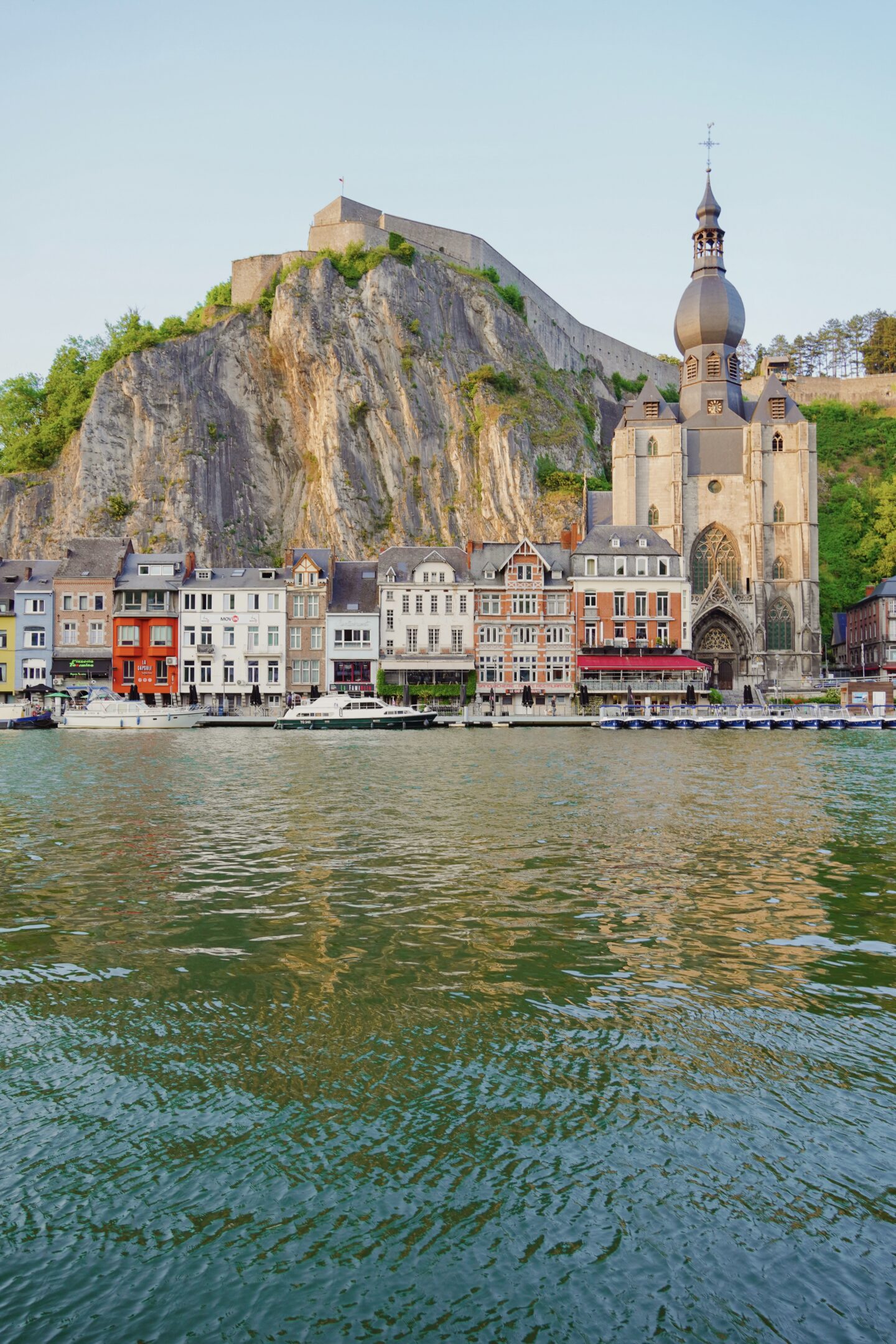view of dinant belgium. colorful Belgian buildings along blue water with cathedral and fortress in background
