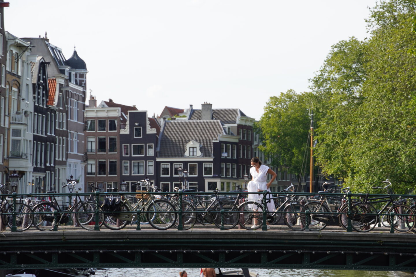 woman in white dress standing on bridge over a canal in amsterdam with typical amsterdam canal homes in background