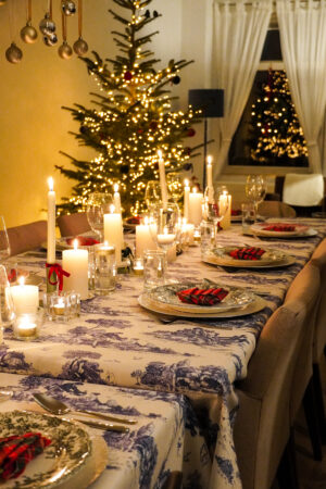 set dinner table for toile and tartan holiday dinner party with lit candles as centerpiece