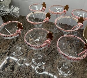 holiday martini glasses decorated with peppermint rims, candy canes, and mini gingerbread man
